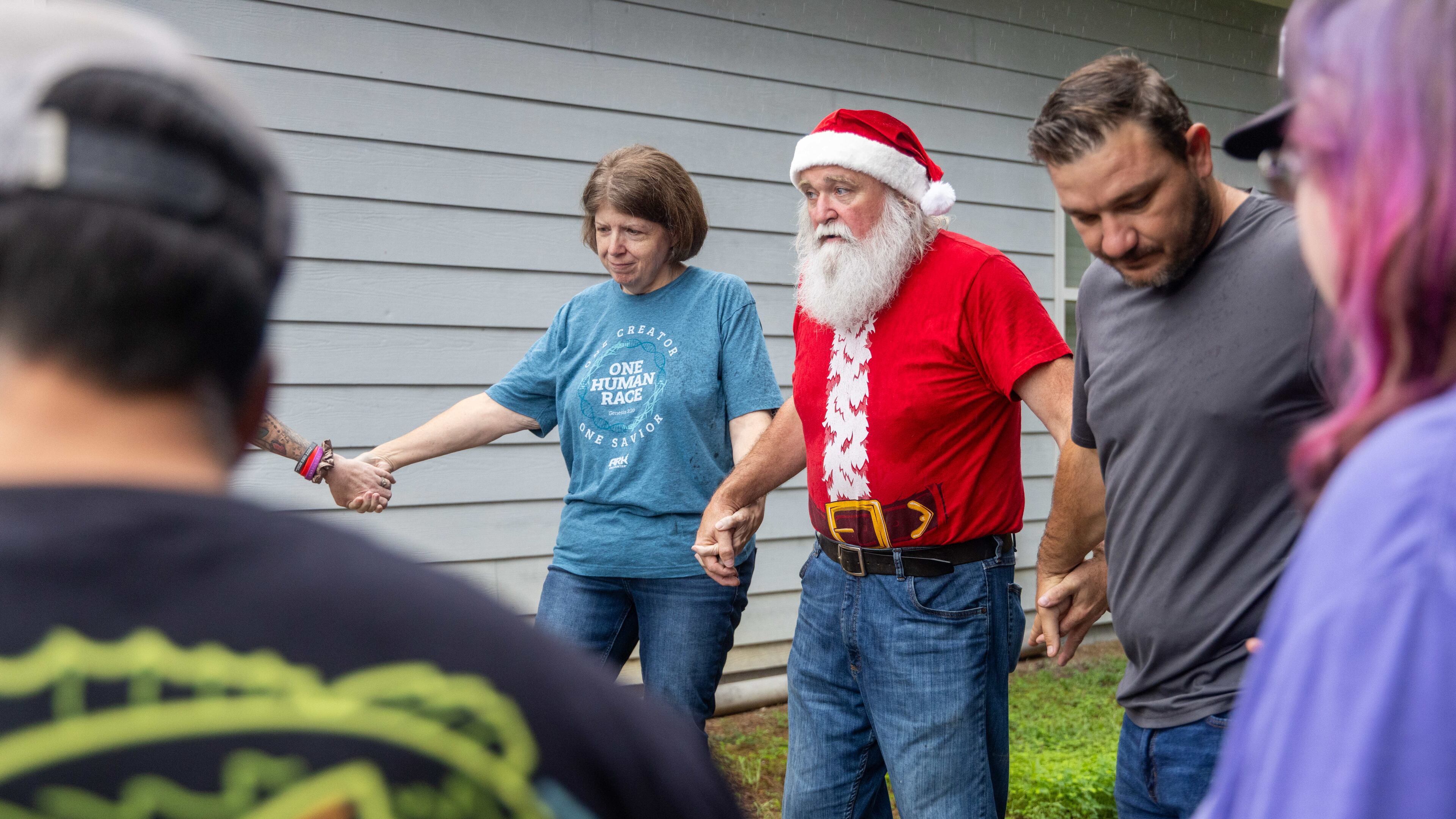 Randy Smith, aka "Santa Randy" (center, in red), prays with volunteers at his Flowery Branch home before heading to a homeless encampment. He leads a group of volunteers from Santa for the Homeless to set up tents with food, clothing and other needs near a homeless encampment in Gainesville. (Phil Skinner for the AJC)