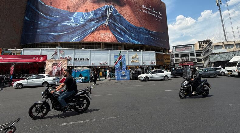 Vehicles drive past a billboard with graphic showing Strait of Hormuz and sewn lips of U.S. President Donald Trump in a square in downtown Tehran, Iran, Saturday, May 2, 2026. (AP Photo/Vahid Salemi)