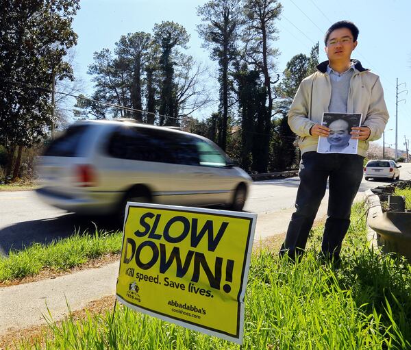 Ke Wu holds a picture of his father Jianchang Wu, who was struck and killed while trying to cross North Decatur Road in Atlanta. Ke Wu is seen here in March 2014, standing at the accident site, where a “slow down” sign had since been placed. The elder Wu and his wife were visiting their son from China. Their son believes the speed the vehicle was traveling contributed to the accident. CURTIS COMPTON / CCOMPTON@AJC.COM