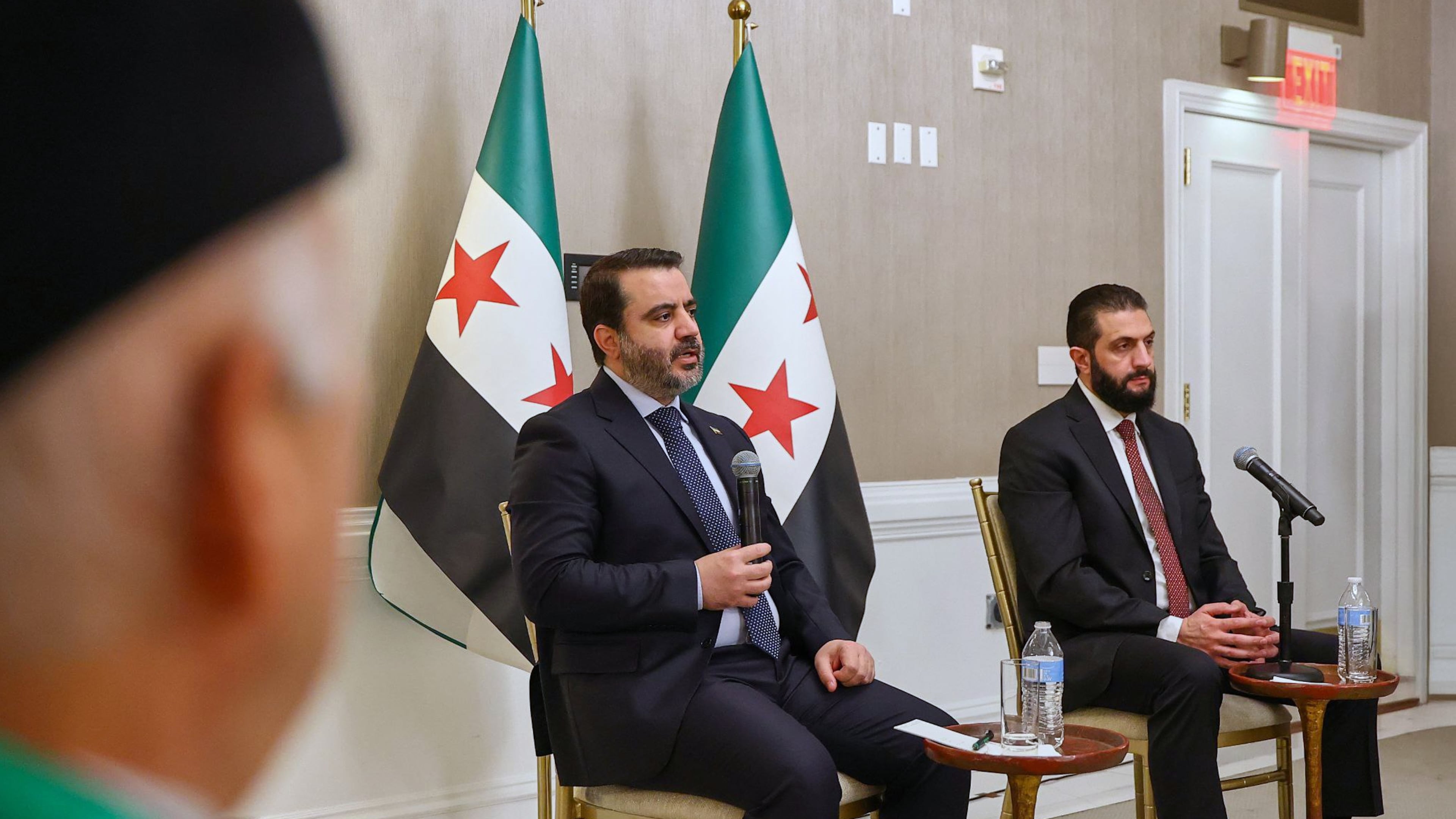 In this photo, released by the Syrian Presidency Press Office, Syrian President Ahmad al-Sharaa, right, listens as Syrian Foreign Minister Asaad al-Shibani, center, speaks during a meeting with representatives of Syrian American organizations in Washington, Saturday, Nov. 8, 2025. (Syrian Presidency Press Office via AP)