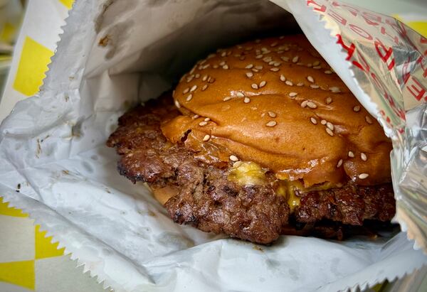 A smashburger in a foil bag with the beef overlapping the bun.