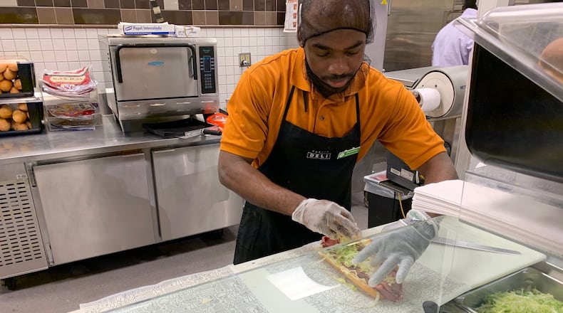 While layoffs are reaching epic levels, many grocery stores are busy. Among the stores that are hiring is Publix. Here, Dominick Ebwele, working the deli at the Shamrock Plaza Publix near Decatur. (CONTRIBUTED BY OLIVIA KING)