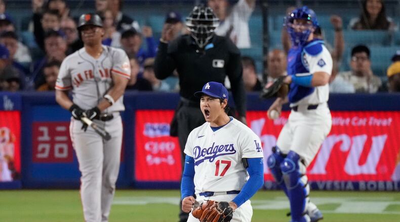 Los Angeles Dodgers two-way player Shohei Ohtani, center, reacts after striking out San Francisco Giants' Rafael Devers, left, as catcher Will Smith gets ready to throw the ball back during the sixth inning of a baseball game Wednesday, May 13, 2026, in Los Angeles. (AP Photo/Mark J. Terrill)