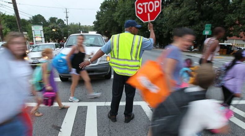 A school crossing guard helps E. Rivers Elementary students and adults cross the street. (AJC File Photo)
