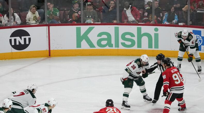 A face-off during the third period of an NHL hockey game between the Chicago Blackhawks and the Minnesota Wild with the Kalshi sign in the background Tuesday, March, 17, 2026, in Chicago. (AP Photo/David Banks)
