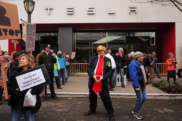 Victoria Millard of the Troublemakers stands in front of a Tesla showroom dressed as President Donald Trump during a protest against Tesla and Elon Musk Saturday, March 29, 2025, in the University District of Seattle. (AP Photo/Lindsey Wasson)