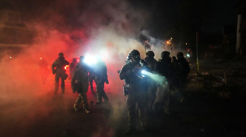 Law enforcement officers stand amid tear gas at the scene of a reported shooting Wednesday, Jan. 14, 2026, in Minneapolis. (AP Photo/Adam Gray)
