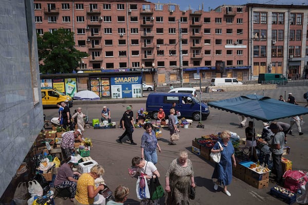 People shop at a street market near a building which was damaged by a Russian attack in Kyiv, Ukraine, on Thursday, July 10, 2025. (AP Photo/Evgeniy Maloletka)