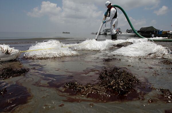 FILE - A worker uses a suction hose to remove oil washed ashore from the Deepwater Horizon spill, in Belle Terre, La., June 9, 2010. (AP Photo/Eric Gay, File)