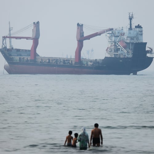 A group of people stands in shallow water as a cargo ship appears anchored in the Strait of Hormuz off Bandar Abbas, Iran, Tuesday, June 30, 2026. (Amirhosein Khorgooi/ISNA via AP)