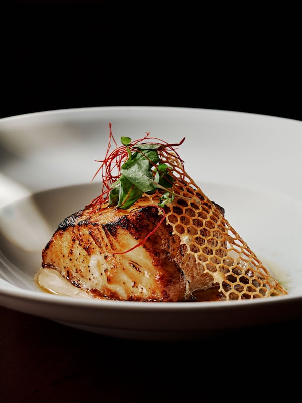 a dish of roasted seabass filet with vegetables and a tuile with a hexagonal designe