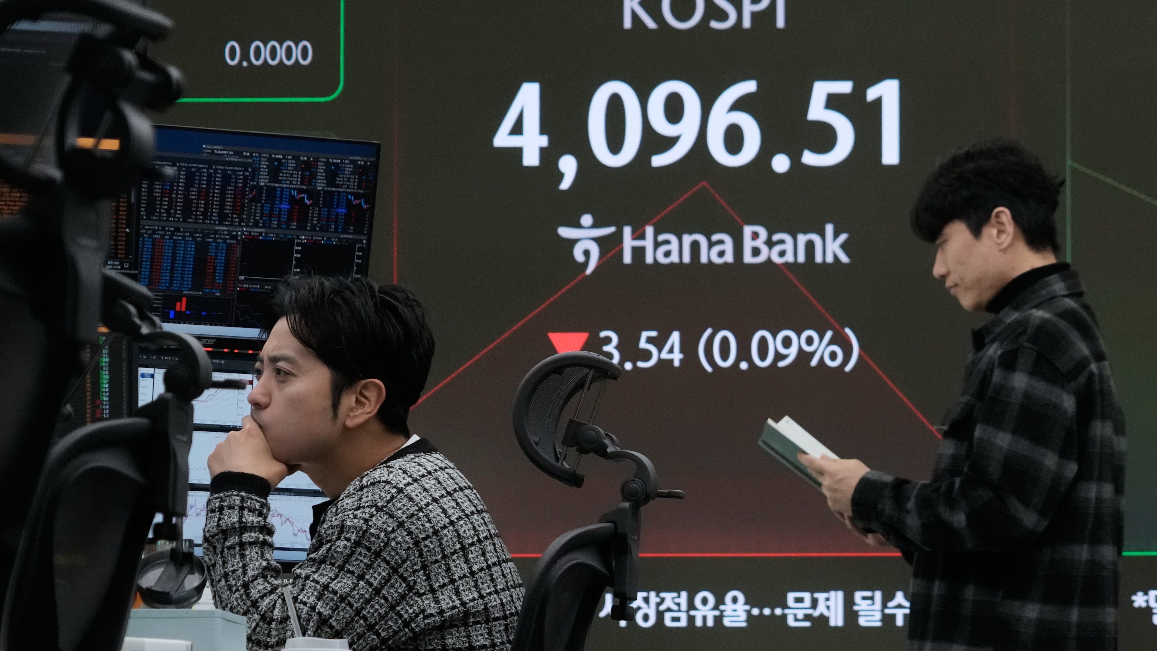 A currency trader watches monitors near a screen showing the Korea Composite Stock Price Index (KOSPI) at the foreign exchange dealing room of the Hana Bank headquarters in Seoul, South Korea, Monday, Dec. 8, 2025. (AP Photo/Ahn Young-joon)