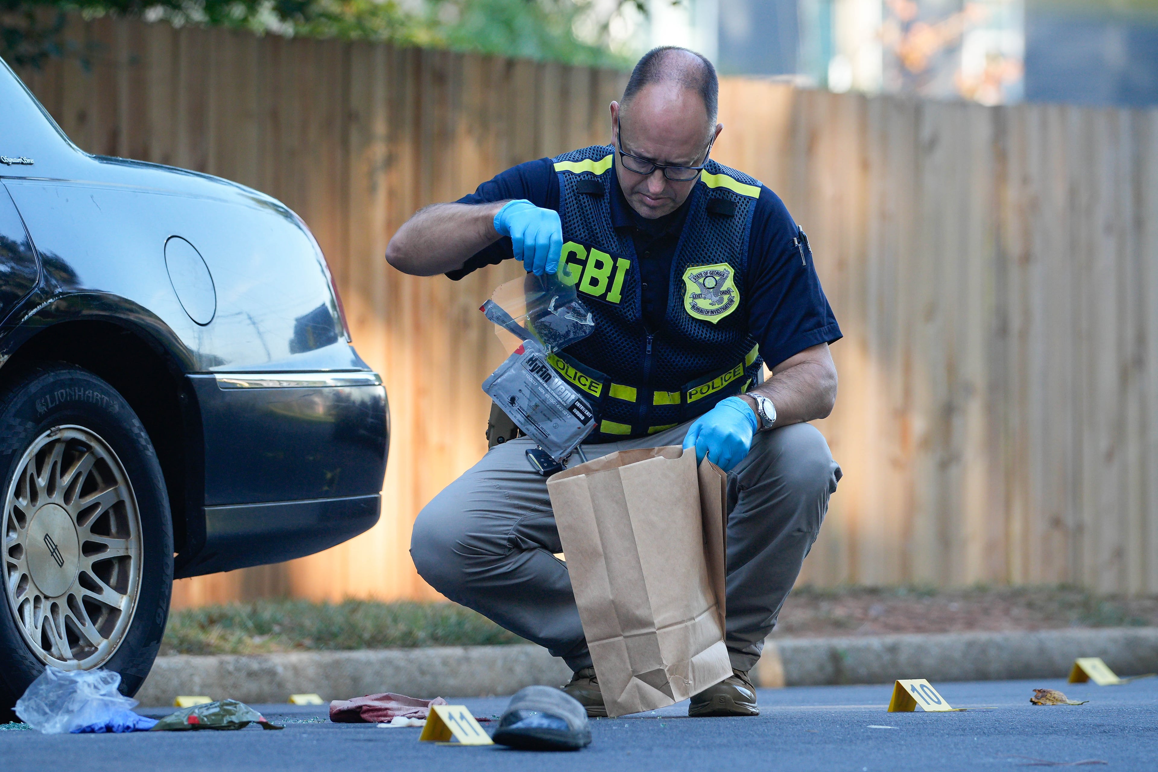 Several evidence markers are scattered about the ground as a GBI investigator collects evidence at the scene of an officer-involved shooting in DeKalb County on Wednesday, Sept. 24, 2025. (Ben Hendren for the AJC)
