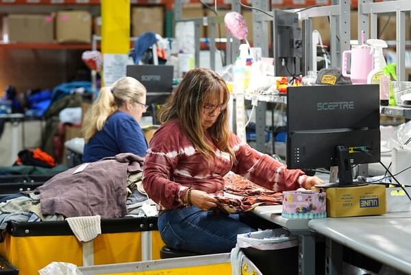 People work amid boxes of returned or overstocked clothing, shoes, boots, coats, packs and other items in a warehouse where the goods are cleaned or repaired before they are marketed on resale platforms in Englewood, Colo., on Thursday, April 17, 2025. (AP Photo/David Zalubowski)