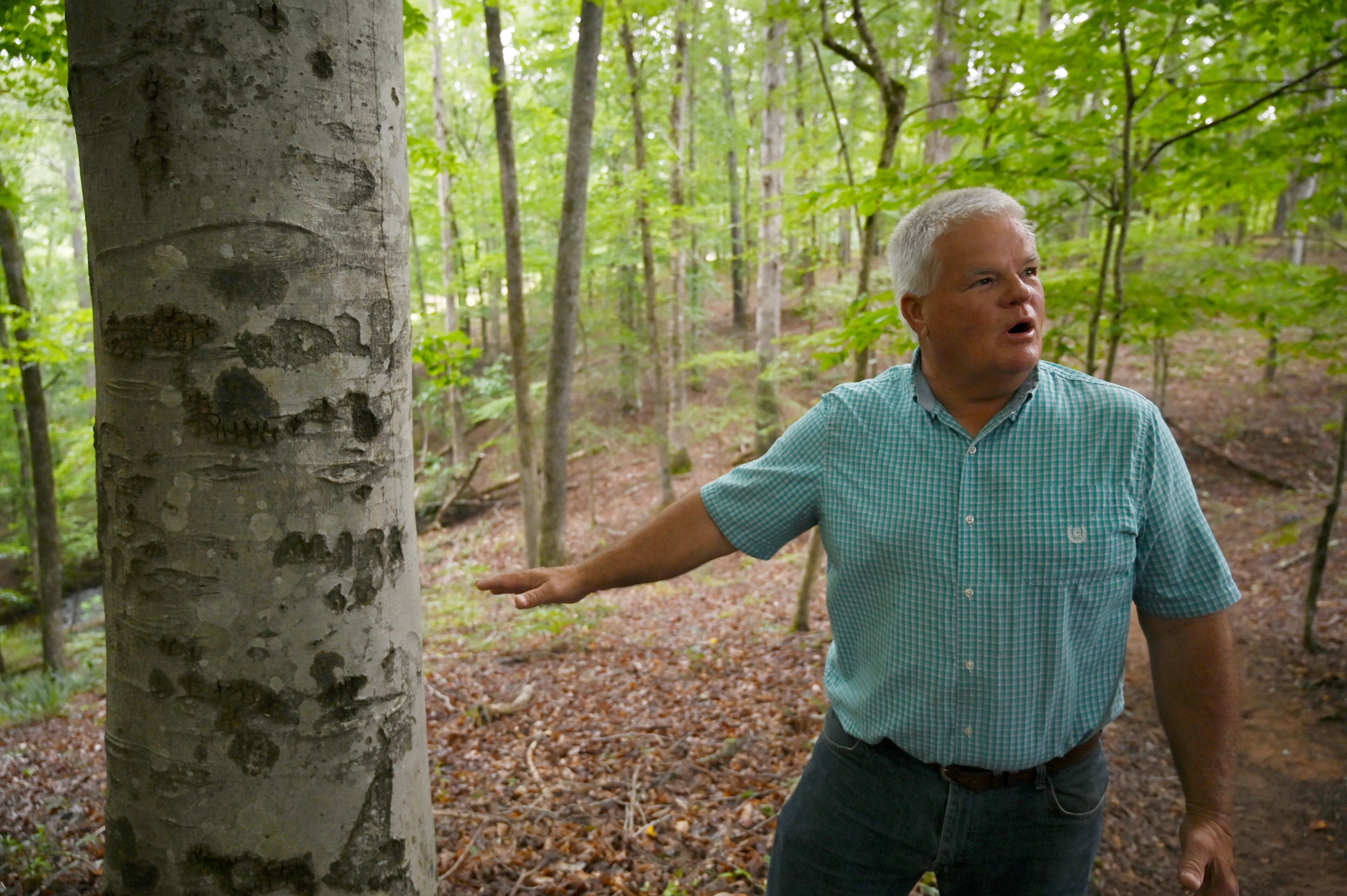 Mark Thomas shows his name carved into a tree by his father, 'Hot' Thomas, at the Thomas Farm Preserve on Wednesday, June 18, 2025, in Watkinsville. Thomas' family owned the property, which is now a preserve, since the 1800s. (Hyosub Shin/AJC)