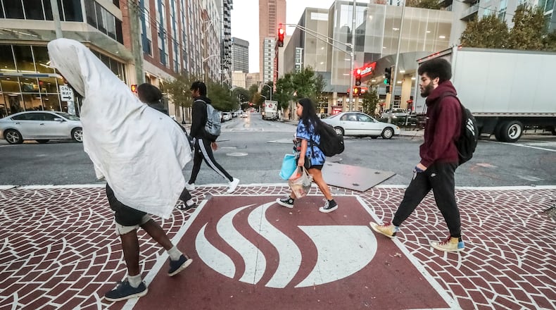 Students and other pedestrians use the crosswalk at the intersection of Piedmont Avenue and John Wesley Dobbs Avenue on Monday, Oct. 30, 2023, after a shooting that killed one woman and wounded three other people, including two students. (John Spink / John.Spink@ajc.com)