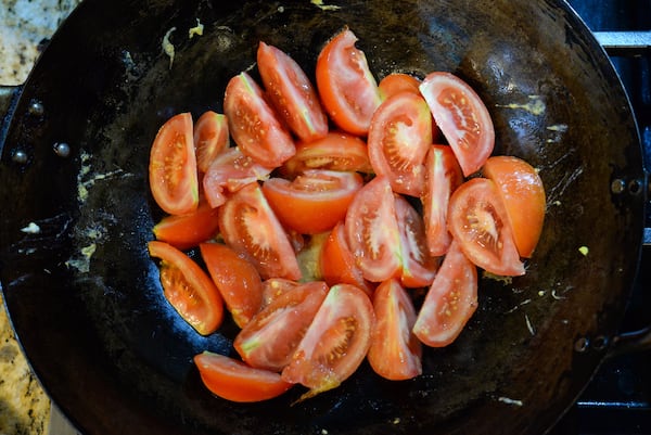 A close-up shot of a well-oiled wok holding tomato wedges.
