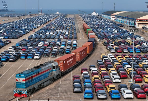 A cargo train moves past new cars waiting for shipment in a port, in Yantai in east China's Shandong province on Wednesday, May 7, 2025. (Chinatopix via AP)