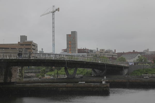 A man walks in the rain across a pedestrian bridge in Providence, R.I. on Thursday, May 22, 2025. (AP Photo/Kimberlee Kruesi)