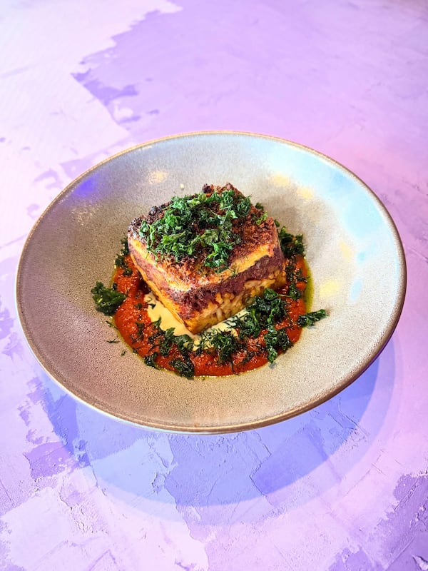 A brightly lit plate of Greek lasagna sits on a pink and blue table