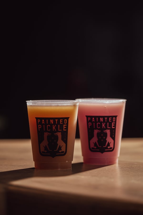 Two plastic cups hold two frozen drinks. They sit on a wooden table. The harsh lighting and strong shadow in the photo implies that the photo was taken in outside in the afternoon sun.