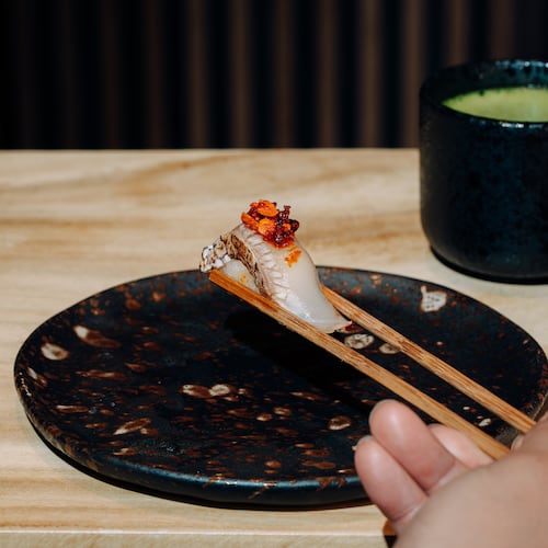 A hand with chopsticks grabs lifts a piece of nigiri off a plate.