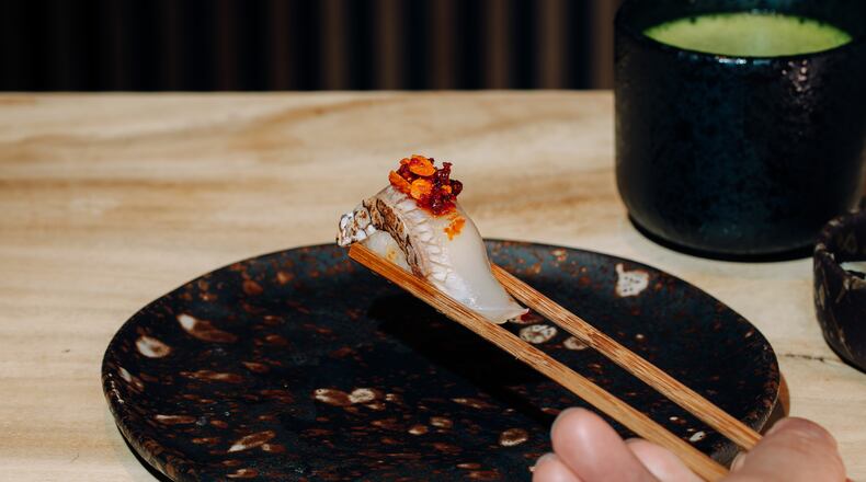 A hand with chopsticks grabs lifts a piece of nigiri off a plate.