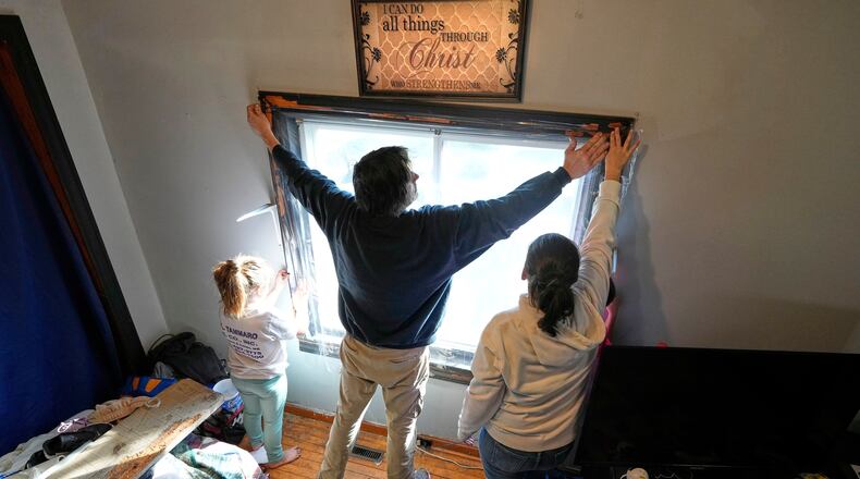 Gerard Berry, along with his wife, Stephanie, and daughter, Brooklynn, cover a bedroom window with plastic, Friday, Nov. 7, 2025, in Baileyville, Maine. (AP Photo/Robert F. Bukaty)