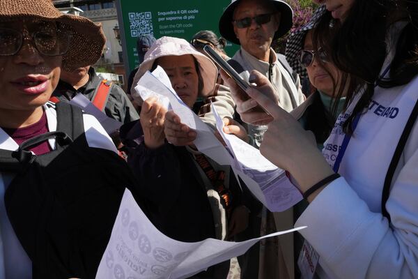 Stewards check tourists' QR codes outside the main train station in Venice, Italy, Friday, April 18, 2025, as the city for a second year is charging day-trippers an arrivals tax. (AP Photo/Antonio Calanni)