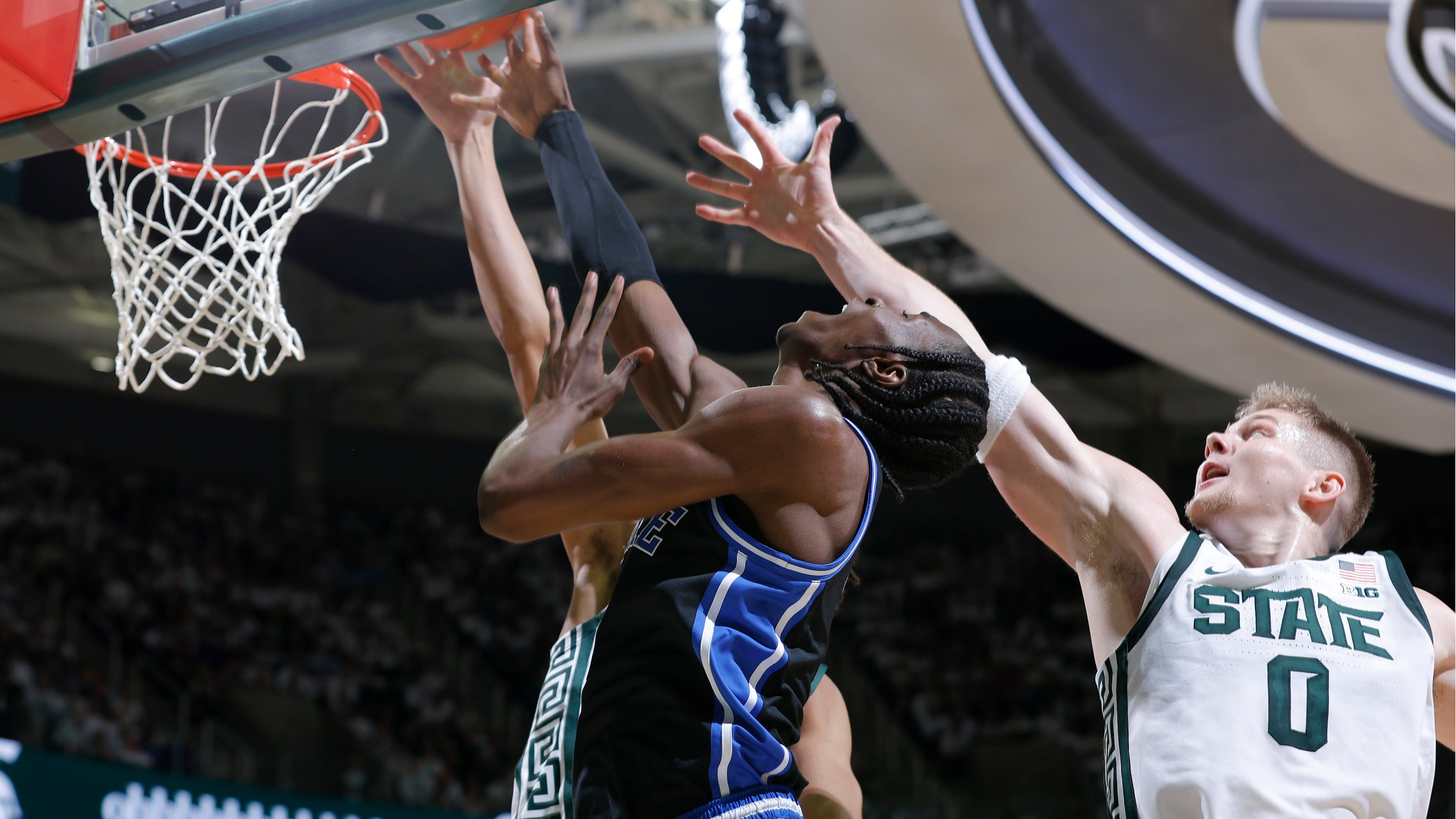 Duke guard Dame Sarr, center, and Michigan State forward Jaxon Kohler (0), right, and forward Jordan Scott, rear, vie for a rebound during the first half of an NCAA college basketball game, Saturday, Dec. 6, 2025, in East Lansing, Mich. (AP Photo/Al Goldis)