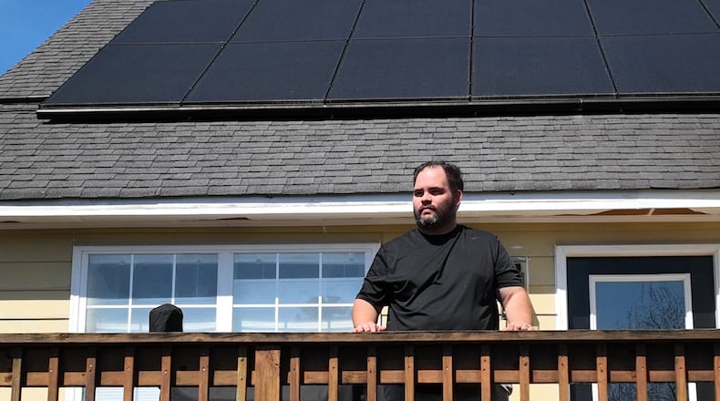 Portrait of Alex Betancourt as solar panels on the roof are shown in background at his home, Friday, March 24, 2023, in Suwanee. Alex Betancourt put solar panels on his roof last year. He received letters from his HOA claiming the panels were an architectural addition that violated the community's rules. Now, they're threatening to remove the panels from his roof. (Hyosub Shin / Hyosub.Shin@ajc.com)