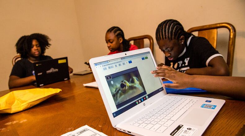 Rakiyah Hill, 10, front right, a 5th grader at McClendon Elementary, learns cell structure on a computer her mother had to buy this month so all children would be able to get their school work done. Raina Hill, 12, back left, a 6th grader at Champion Middle School uses the only DeKalb County computer they have, while Rihanna Hill,13, in red, an 8th grader at Champion Middle School uses a tablet to do school work and sister, Roniyah Hill, black shirt braids,15, a 10th grader at Martin Luther King High School uses her phone to look up definitions.(Jenni Girtman for Atlanta Journal Constitution)