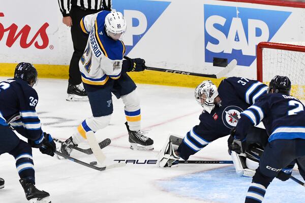 Winnipeg Jets goaltender Connor Hellebuyck (37) makes a save against St. Louis Blues' Jimmy Snuggerud (21) during the third period of Game 2 of a first-round NHL hockey playoff series in Winnipeg, Manitoba, Monday April 21, 2025. (Fred Greenslade/The Canadian Press via AP)