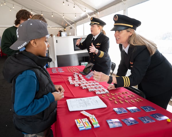 Two women in pilot uniforms talk to a group of kids and hand out airplane pins.