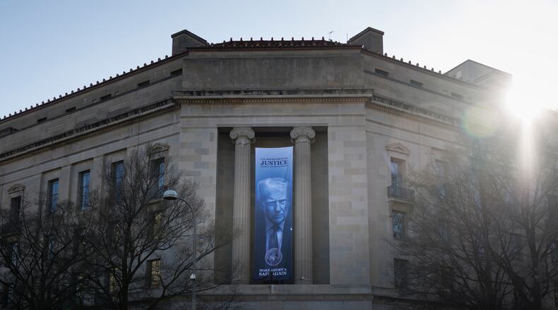 A banner of President Donald Trump hangs outside the U.S. Department of Justice on Saturday, March 21, 2026, in Washington. (AP Photo/Tom Brenner)