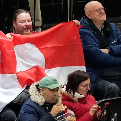Fans hold Greenland national flag before a preliminary round match of men's ice hockey between United States and Denmark at the 2026 Winter Olympics, in Milan, Italy, Saturday, Feb. 14, 2026. (AP Photo/Hassan Ammar)