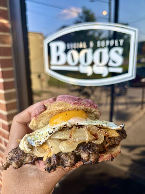 Sandwich held in front of the Bogos restaurant sign.