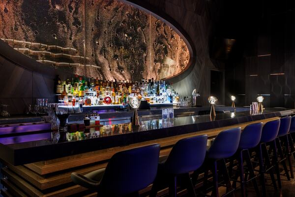 A modern, dimly lit bar with a large, oval window revealing an abstract, moonscape-like wall