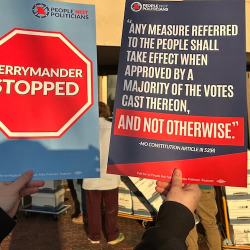 An opponent of new Missouri congressional districts approved by the Republican-led legislature holds signs outside the secretary of state's office in Jefferson City, Missouri, on Tuesday, Dec. 9, 2025, as petitions calling for a referendum election are delivered. (AP Photo/David A. Lieb)