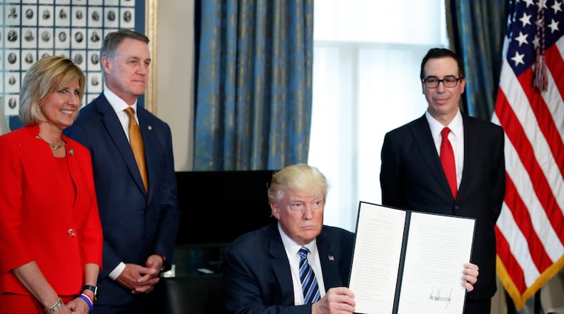 President Donald Trump, accompanied by, from left, Rep. Claudia Tenney, R-N.Y., Sen. David Perdue, R-Ga., and Treasury Secretary Steve Mnuchin, holds up a signed Executive Order, Friday, April 21, 2017, at the Treasury Department in Washington. (AP Photo/Alex Brandon)