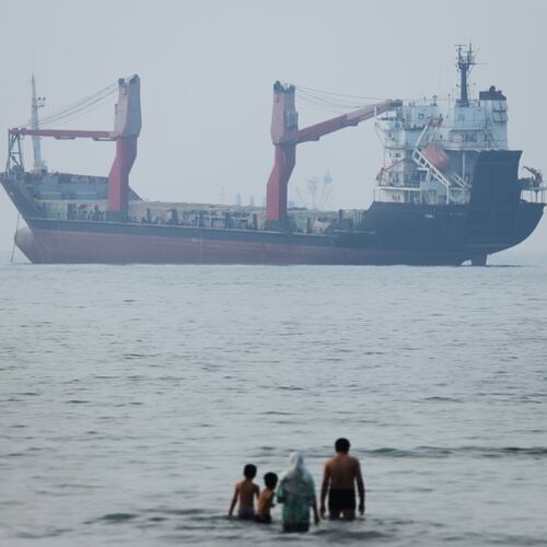 A group of people stands in shallow water as a cargo ship appears anchored in the Strait of Hormuz off Bandar Abbas, Iran, Tuesday, June 30, 2026. (Amirhosein Khorgooi/ISNA via AP)
