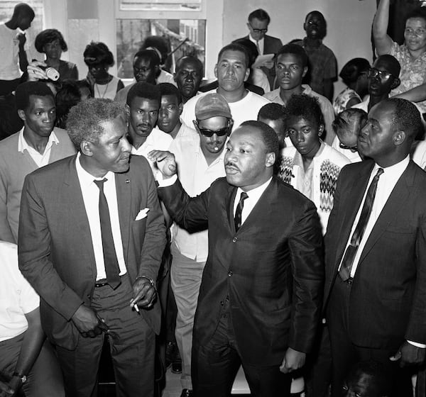 FILE - Dr. Martin Luther King Jr., center, with his aide, Bayard Rustin, left, addresses a gathering in the riot-torn area of Los Angeles, in one of many meetings King attended in an attempt to solve the problems connected with the uprising, Aug. 18, 1965. (AP Photo/Don Brinn, File)