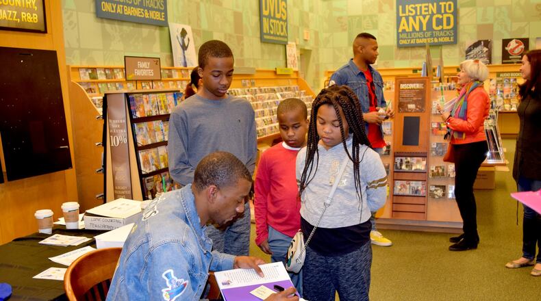 (From left) Will, Preston and Gabby Flournoy watch as NFL player Malcolm Mitchell signs their copies of his book, “The Magician’s Hat.” (Alexis Stevens/astevens@ajc.com)