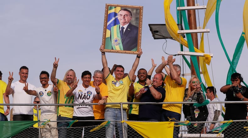 Opposition presidential candidate Flavio Bolsonaro holds a photo of his father, former President Jair Bolsonaro, as he rides a boat during a campaign rally ahead of the October general elections in Angra dos Reis, Rio de Janeiro state, Brazil, Saturday, Aug. 29, 2026. (AP Photo/Bruna Prado)