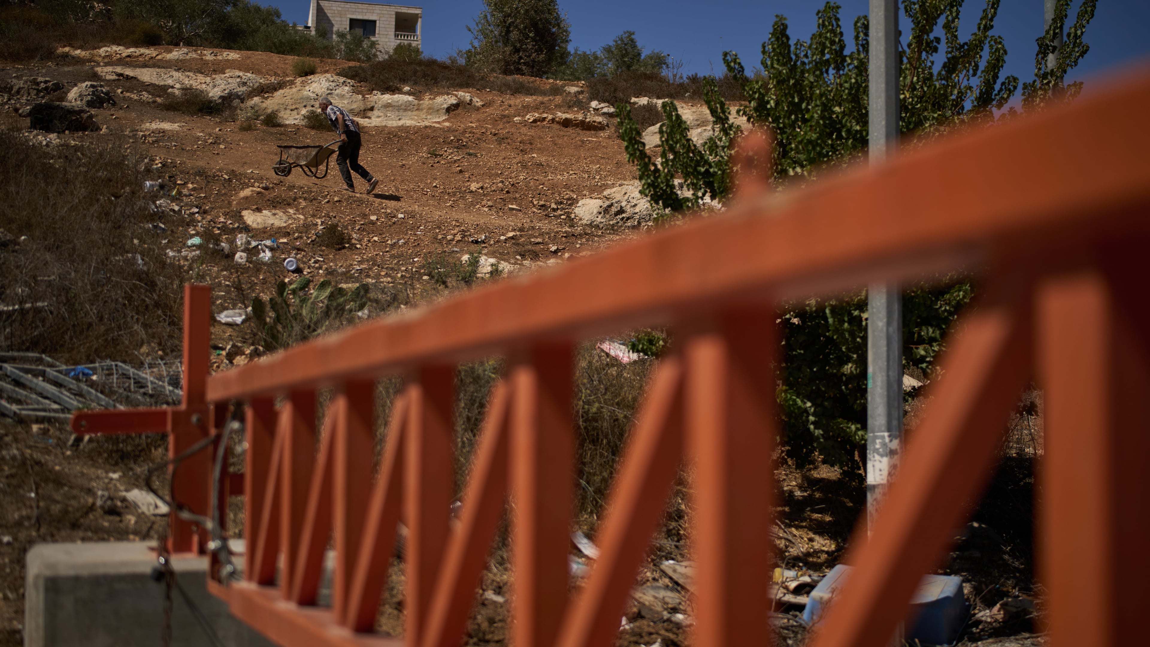 A Palestinian man pushes a wheelbarrow past a closed gate set up by Israeli authorities that blocks an entrance to the West Bank village of Sinjil, Tuesday, Sept. 30, 2025. (AP Photo/Leo Correa)