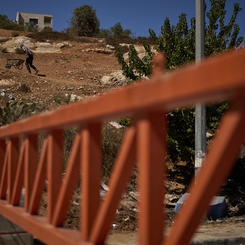 A Palestinian man pushes a wheelbarrow past a closed gate set up by Israeli authorities that blocks an entrance to the West Bank village of Sinjil, Tuesday, Sept. 30, 2025. (AP Photo/Leo Correa)
