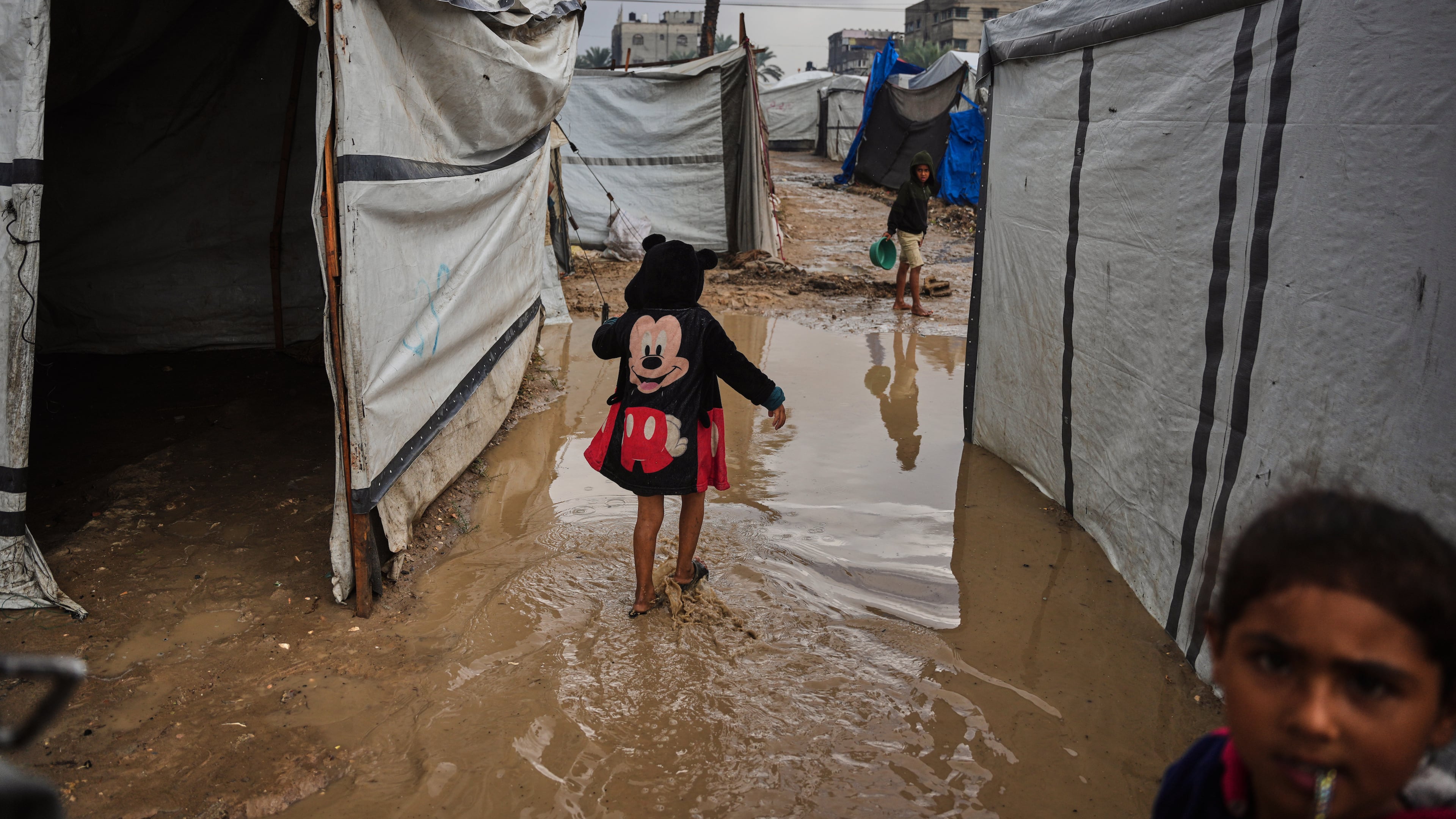 Palestinians walk through a flooded temporary tent camp after heavy rainfall in Deir al-Balah, central Gaza Strip, Tuesday, Nov. 25, 2025. (AP Photo/Abdel Kareem Hana)