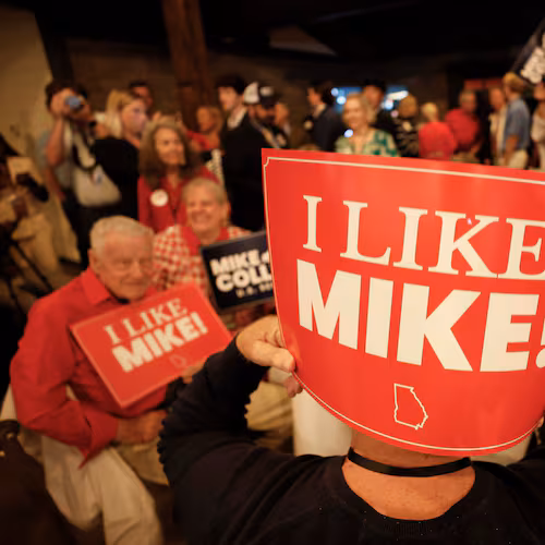 Supporters of U.S. Rep. Mike Collins hold banners as they watch him arrive on stage for his speech during the runoff election watch party in Jackson last month. (Miguel Martinez/AJC)