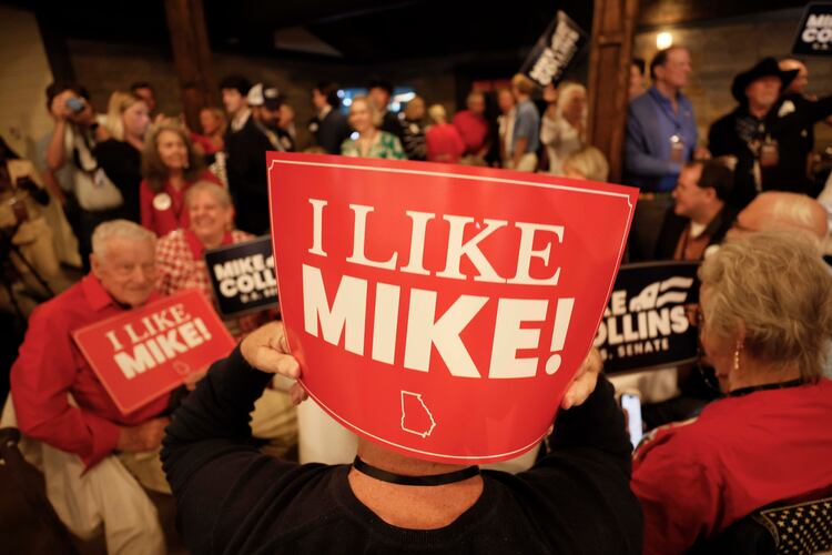 Supporters of U.S. Rep. Mike Collins hold banners as they watch him arrive on stage for his speech during the runoff election watch party in Jackson last month. (Miguel Martinez/AJC)