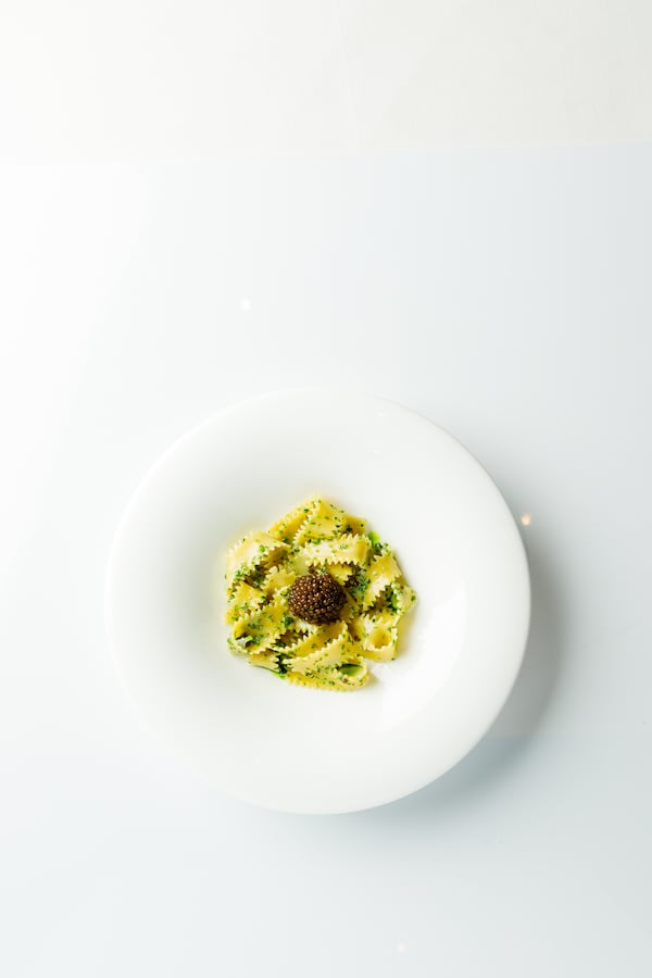 A white plate holds a small pile of pasta dotted with chives and topped with a bump of caviar.